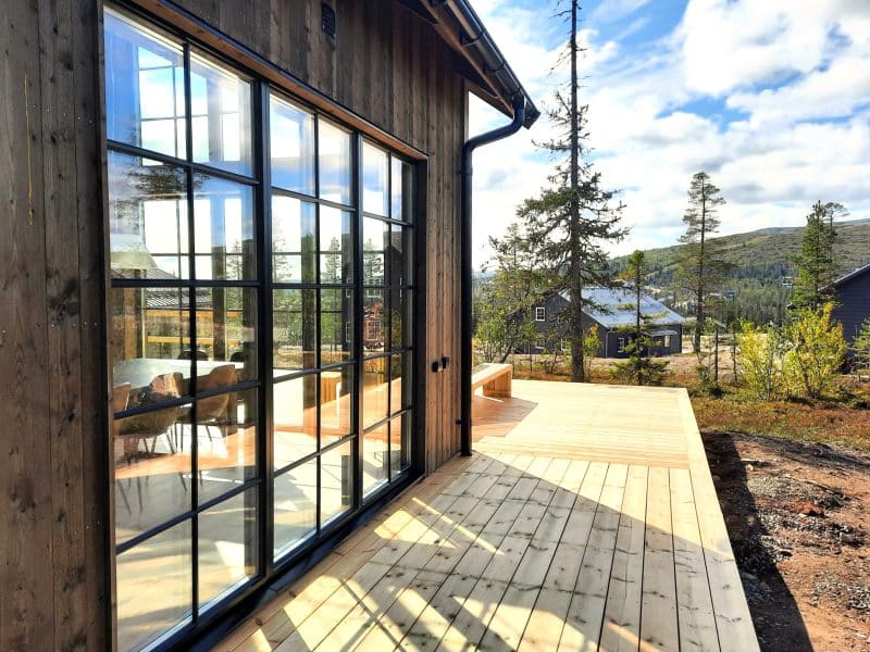 Modern mountain house with large glass sections and a large sun deck with a view of the vast mountain environment.