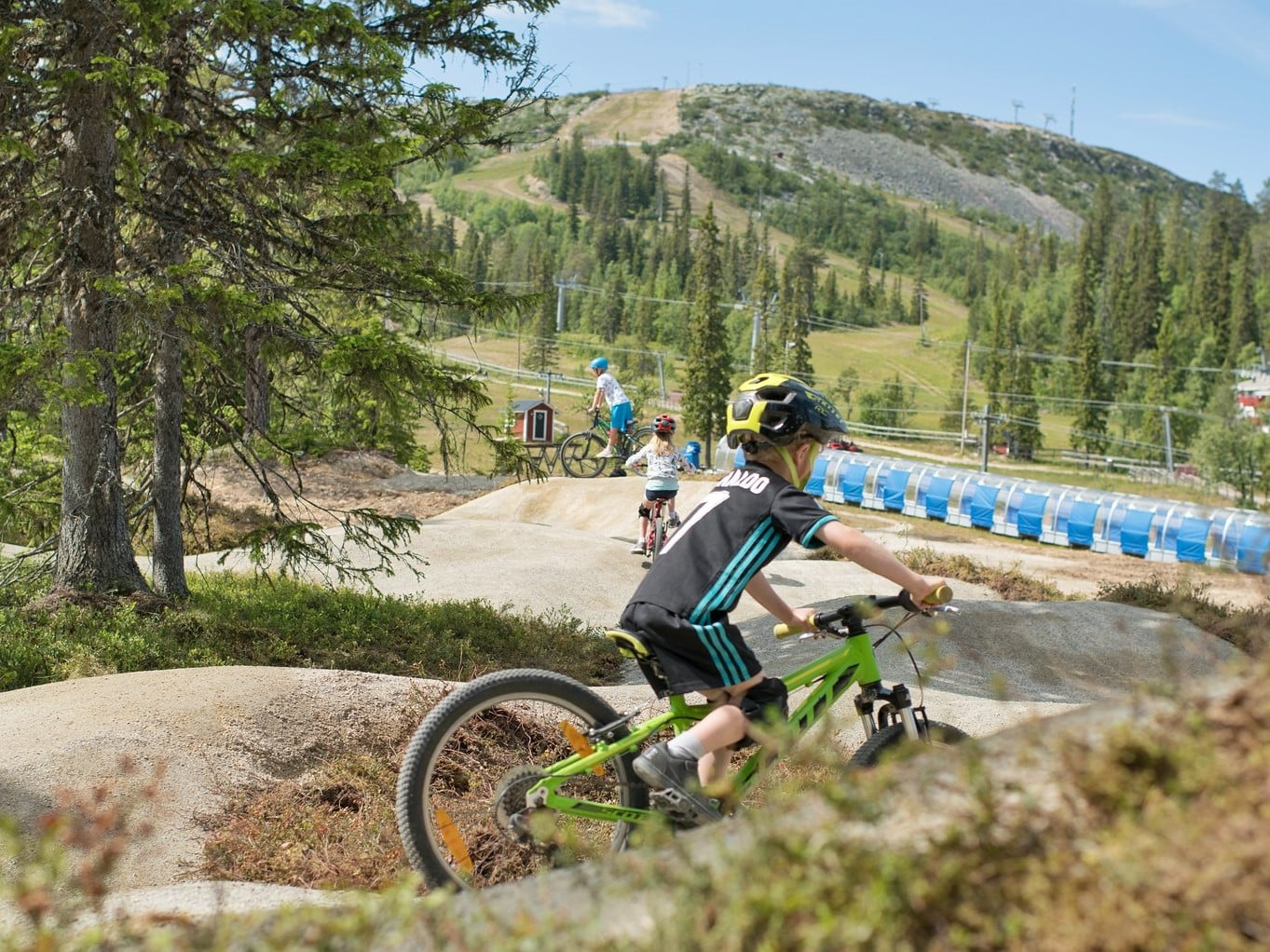 Pojke i hjälm, shorts och t-shirt som cyklar på en grön MTB-cykel på trails nedanför Hovdefjället.