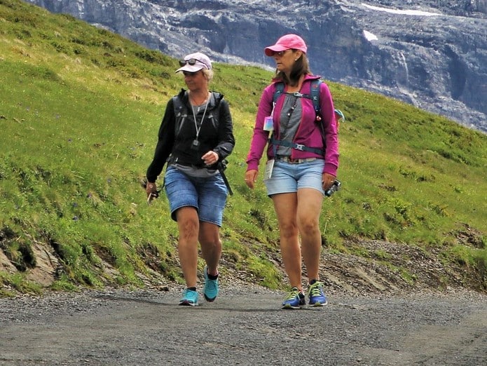 Two women in caps and sunglasses hiking in the mountains.