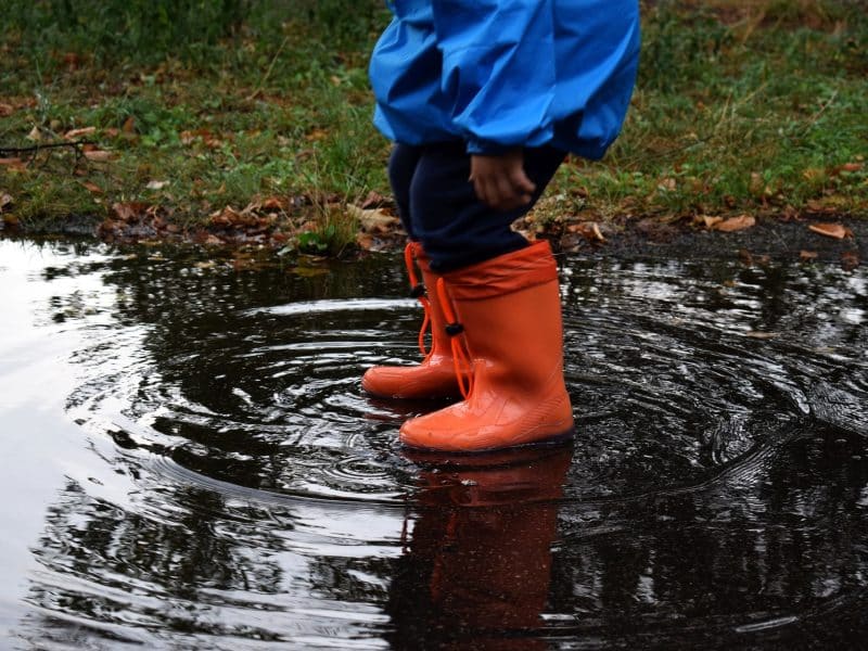 Puddle of water where a child is standing. You only see the orange rubber boots and blue galoon trousers.